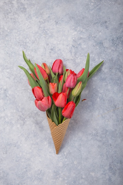 Tulipanes rojos hermosos en un cono de galleta de helado sobre un fondo concreto. Idea conceptual de un regalo de flores. Humor de primavera