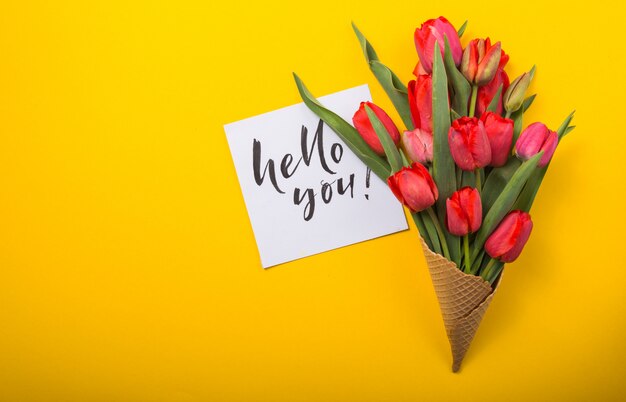 Tulipanes rojos hermosos en un cono de galleta de helado con tarjeta de tinta sobre un fondo de color amarillo. Idea conceptual de un regalo de flores. Humor de primavera