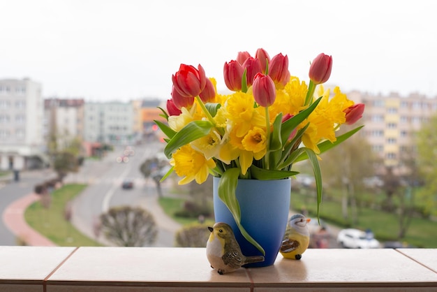 Tulipanes rojos y narcisos amarillos en un hermoso ramo primaveral Ramo floral primaveral en una ventana contra la vista de la ciudad