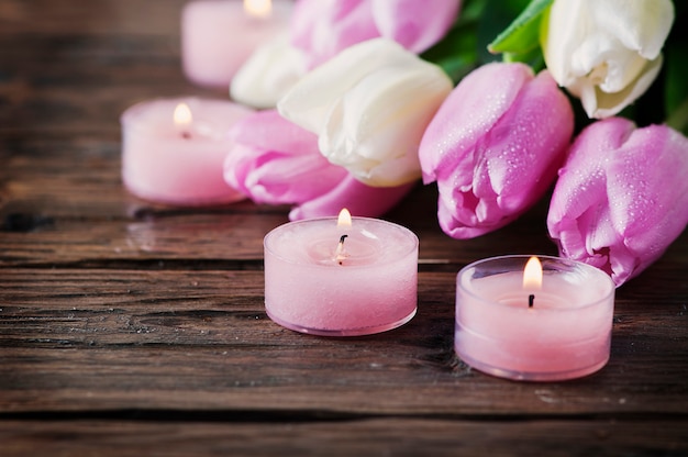 Tulipanes rosados y blancos y velas en la mesa de madera