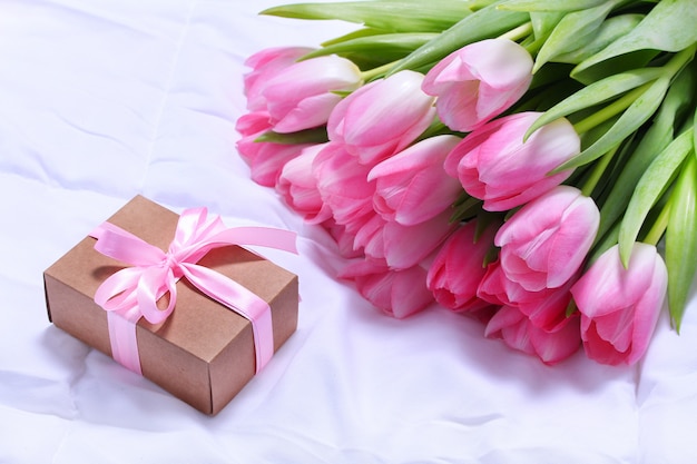 Tulipanes rosados y caja de regalo artesanal en sábana blanca en cama.