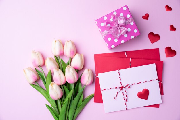 Tulipanes rosados, caja de regalo con corazón rojo y cubierta de carta rosa roja sobre fondo rosa