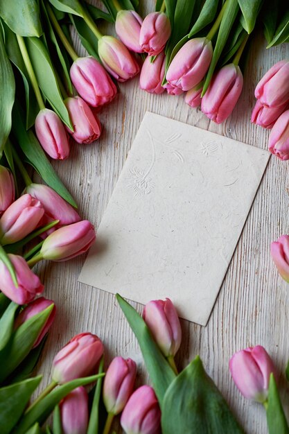 Tulipanes rosados dispersos al azar yacen sobre un sobre Kraft de textura de madera