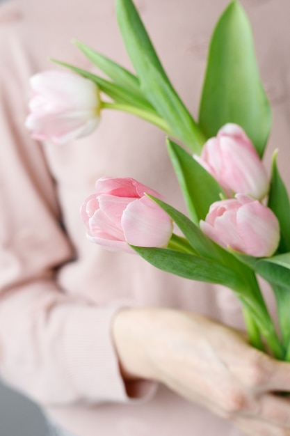 Foto tulipanes rosados con hojas verdes en un vaso de vidrio mujer sosteniendo tulipanes en sus manos floristería