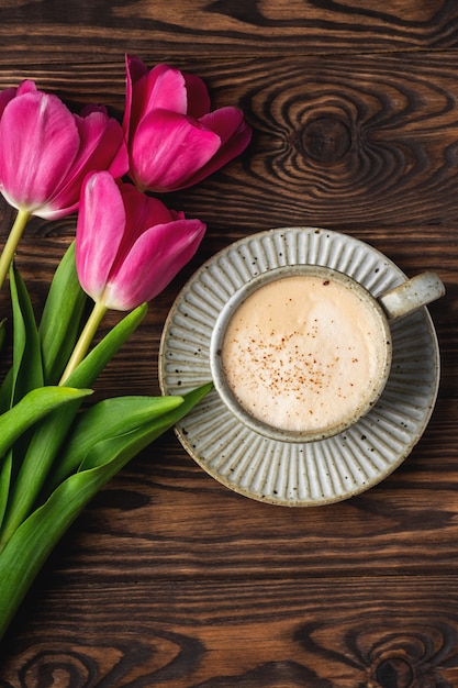 Tulipanes rosados, taza con café en una mesa de madera, espacio de copia