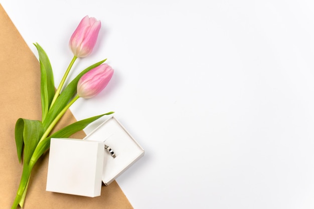 Tulipanes rosas con anillo como regalo sobre fondo blanco con papel artesanal