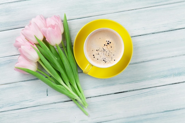 Tulipanes rosas y taza de café en la mesa de madera