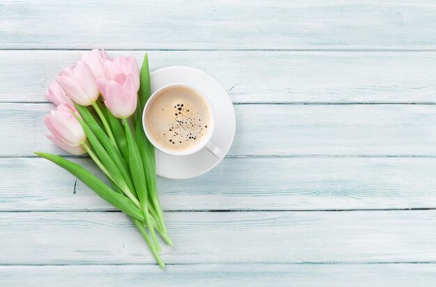 Tulipanes rosas y taza de café en la mesa de madera