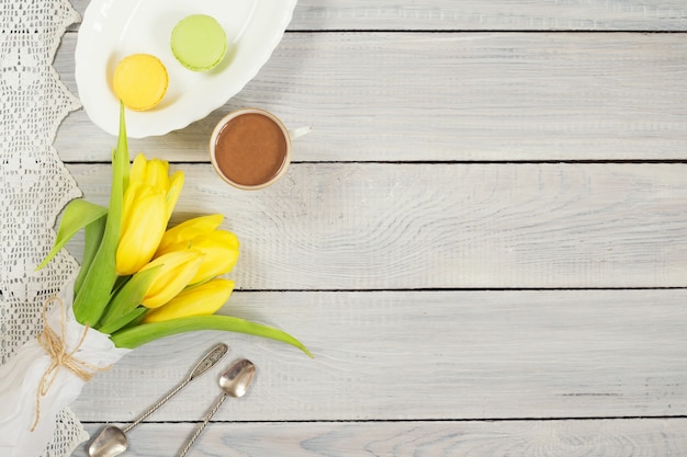 Tulipas amarelas, chocolate e macarons em uma mesa de madeira branca