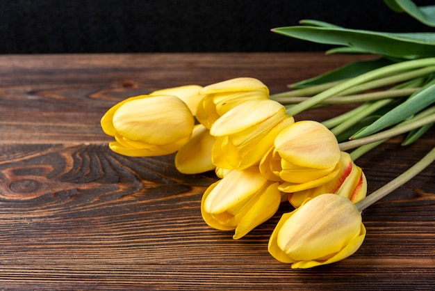 Tulipas amarelas na mesa de madeira escura.