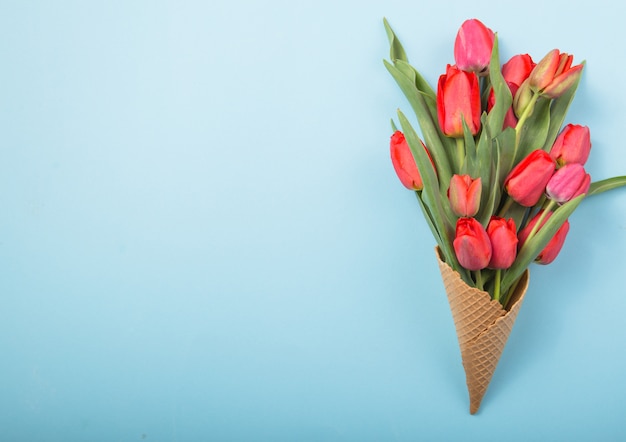 Tulipas bonitas vermelhas em um cone de waffle de sorvete com cartão dia da mulher em um fundo de concreto. Idéia conceitual de um presente de flor. Humor de primavera
