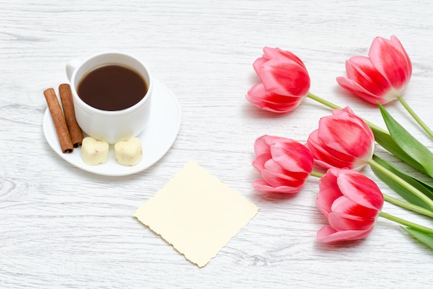 Tulipas cor de rosa, caneca de café e canela, luz de fundo de madeira.