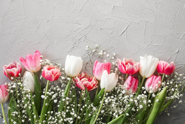 Tulipas cor de rosa e buquê de flores brancas de gypsophila em um elegante fundo de pedra cinza Conceito de comemoração de aniversário do Dia das Mães Copiar espaço para texto