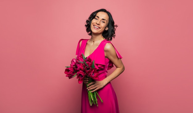 Foto tulipas cor de rosa. foto de close-up de uma senhora alegre em um lindo vestido magenta, que está sorrindo, enquanto segura um monte de tulipas roxas.