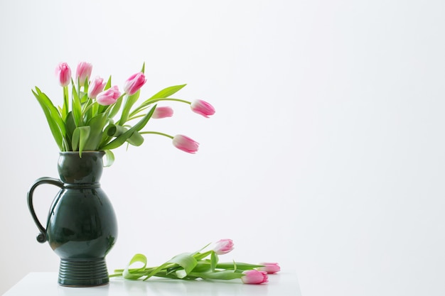 Tulipas cor de rosa no jarro verde sobre fundo branco