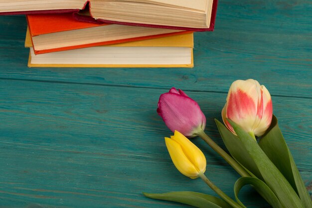 Tulipas de flores e livros em uma mesa de madeira azul