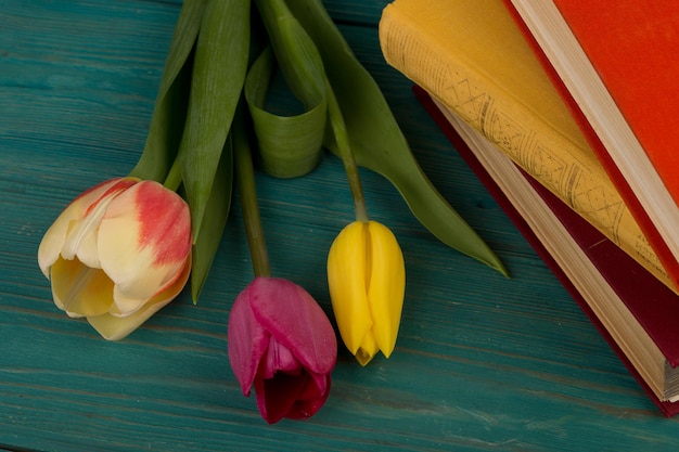 Tulipas de flores e livros em uma mesa de madeira azul