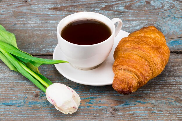 Foto tulipas e xícara de café e croissant na mesa de madeira. vista superior com espaço de cópia.