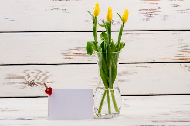 Tulipas em um vaso perto de papel cartão com coração perto de flores compartilham o clima festivo de amor e alegria por toda parte