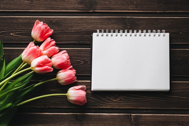 Tulipas flores cor de rosa com o bloco de notas em branco na mesa de madeira para cartão