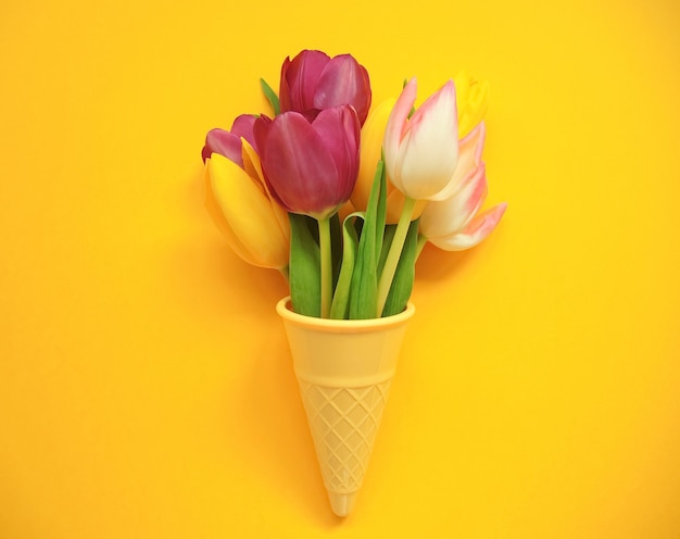 Tulipas multicoloridas em cone de plástico para a Páscoa ou o dia da mulher em fundo amarelo.