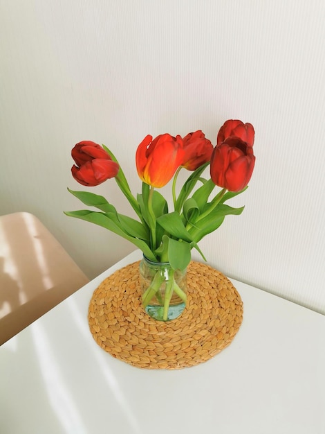 Tulipas vermelhas da primavera em uma mesa branca em um tapete de vime Composição minimalista com flores