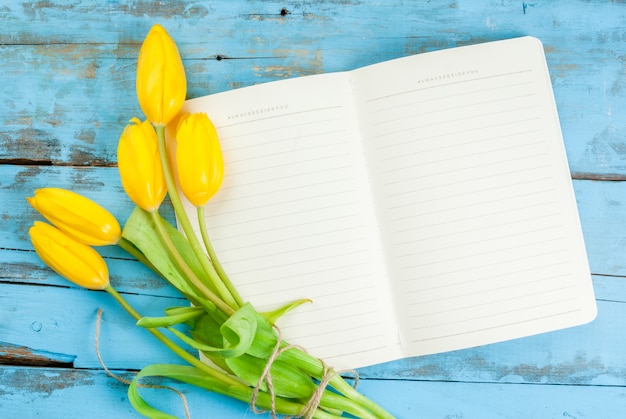 Tulpen und Notizbuch auf blauem Tisch