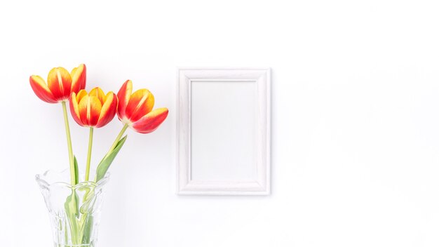 Tulpenblume in Glasvase mit Bilderrahmen auf weißer Wand, Muttertagsdekorkonzept.