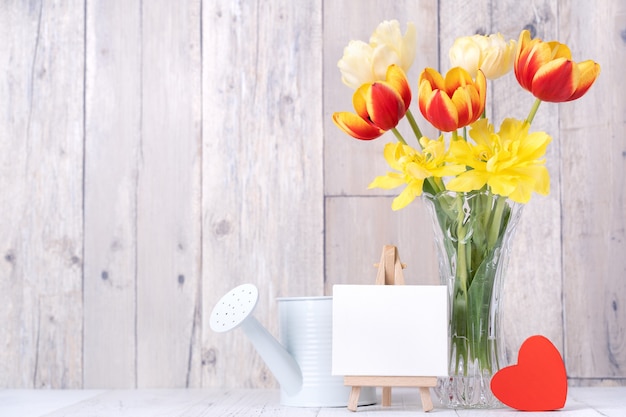 Tulpenblume in Glasvase mit Bilderrahmendekor auf Holztischhintergrundwand zu Hause, Nahaufnahme, Designkonzept zum Muttertag.