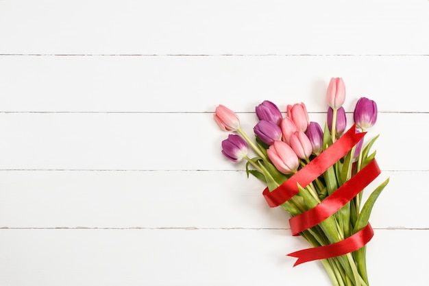 Tulpenblumenstrauß mit rotem Band auf weißem hölzernem Hintergrund. Valentinstag Hintergrund