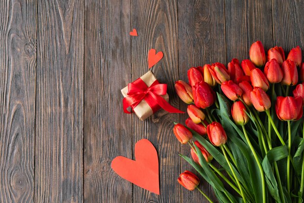 Tulpenbüchel mit Geschenkkiste und roten Herzen auf Holzgrund
