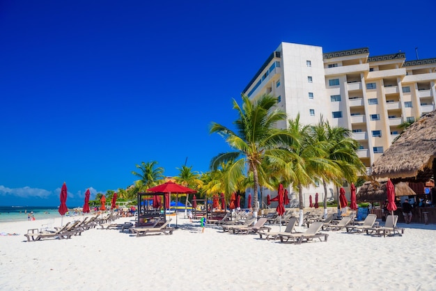 Tumbonas con palmeras cerca del hotel en la playa de arena en un día soleado en Cancún Yukatan México