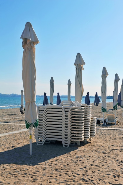 Tumbonas plegadas y sombrillas cerradas en una playa de arena desierta en la mañana.