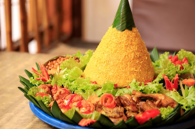 Tumpeng de arroz amarelo, arroz com forma de cone, feito de arroz e cúrcuma, acompanhado de vários acompanhamentos, como frango frito, ovo, tempeh, tofu e pasta de pimenta