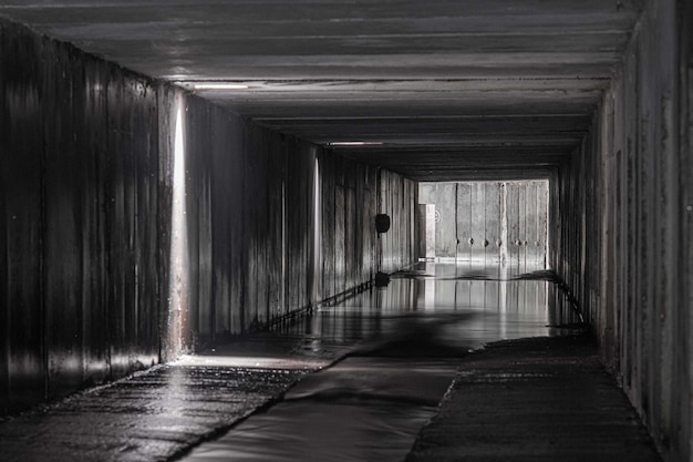 Túnel de concreto retangular de um coletor de drenagem com aberturas para receptores de chuva através dos quais brilha a luz