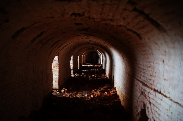 Túnel de ladrillo de miedo en la oscuridad y algo de luz.