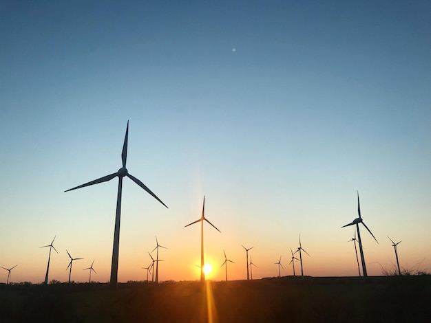 Turbinas eólicas em campo contra céu limpo durante o pôr do sol