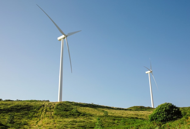 Turbinas de viento en colinas que generan electricidad sobre un cielo azul. Concepto de producción de energía limpia y ecológica.