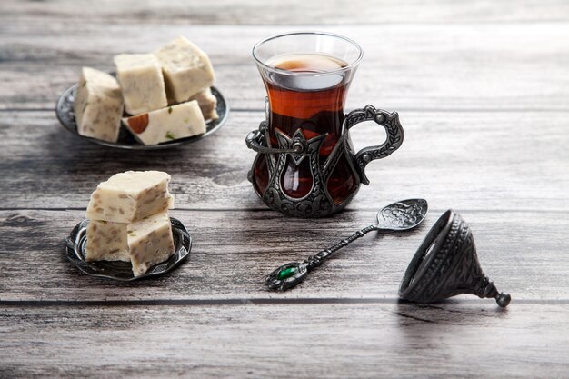 Turetius un vaso de té, una cuchara de metal y halva de girasol con almendras y pistachos se encuentra sobre un fondo de madera.