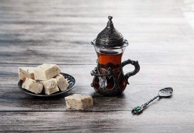 Turetius un vaso de té, una cuchara de metal y halva de girasol con almendras y pistachos se encuentra sobre un fondo de madera.