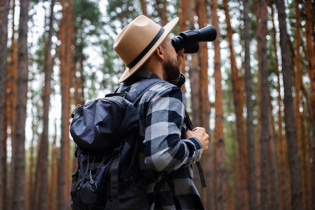 Turismo masculino olhando através de binóculos na floresta.