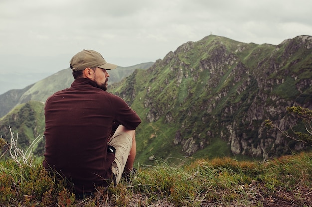 Turismo, montañas, estilo de vida, naturaleza, concepto de personas - Joven parado en la cima del acantilado en las montañas de verano al atardecer y disfrutando de la vista de la naturaleza