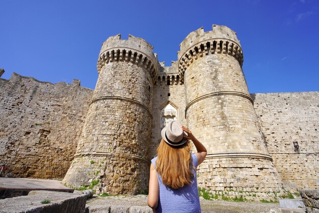 Turismo na Grécia Vista traseira da garota turista andando pela entrada principal do Portão Marinho para a cidade de Rodes a partir do porto Grécia Patrimônio mundial da Unesco