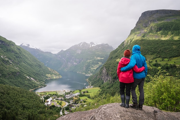 Turismo en noruega. una joven pareja disfrutando de una vista increíble de un fiordo y un valle montañoso. pueblo turístico de geiranger y geirangerfjord