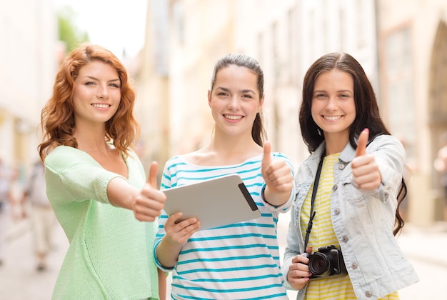 turismo, viagens, lazer, férias e conceito de amizade - adolescentes sorridentes com computador tablet pc e câmera mostrando os polegares