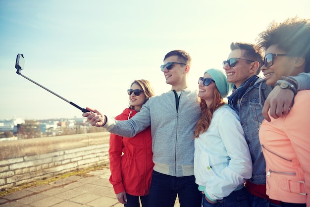 turismo, viagens, pessoas, lazer e conceito de tecnologia - grupo de amigos adolescentes sorridentes tomando selfie com smartphone e monopé na rua da cidade