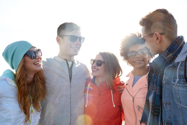 turismo, viajes, gente, ocio y concepto adolescente - grupo de amigos felices con gafas de sol abrazándose y hablando en las calles de la ciudad