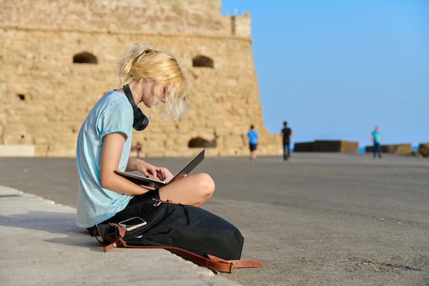 Turista adolescente que usa una computadora portátil antigua fortaleza histórica europea de fondo