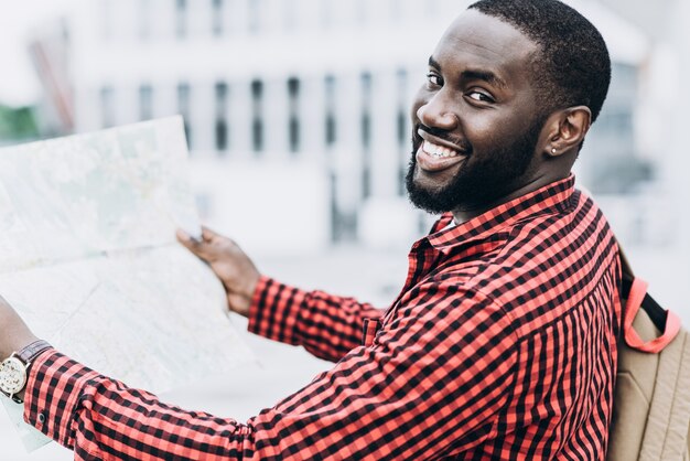 Turista afro-americano bonito e feliz com mapa na cidade moderna