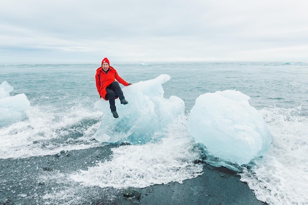 Un turista alegre en una chaqueta roja se asienta sobre un gran trozo de hielo en la laguna de Jokulsarlon .Islandia